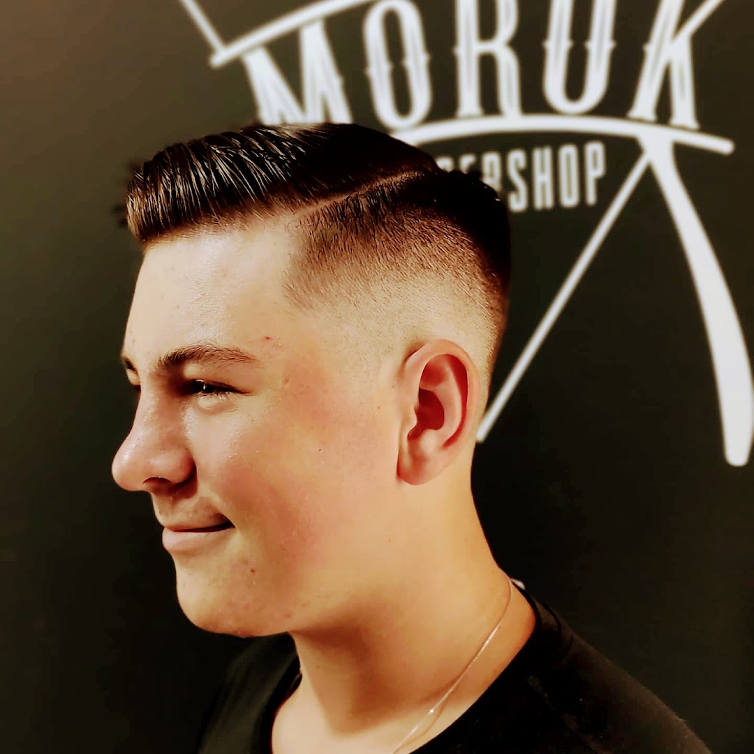 Corte degradê finalizado com o logo da Moruk Barbershop ao fundo